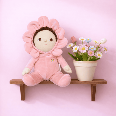 Pink flower plush doll seated on a wooden shelf beside a potted bouquet, from Dinky Dinkum Dolls, a cuddly gift for babies and kids.