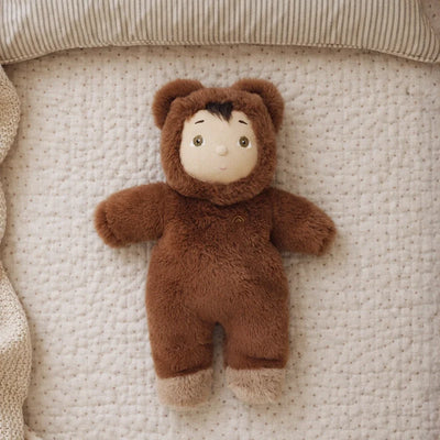 Brown bear plush doll named Bobby Bear lying on a soft quilted bed, with fuzzy ears, embroidered features, and a cozy snuggly design from Cozy Dinkums