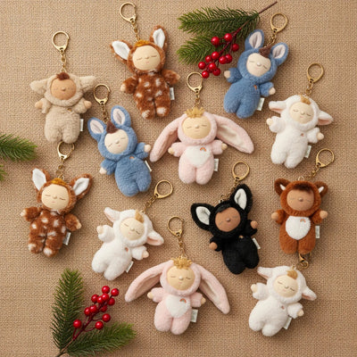 Black cat plush bag charm with a gold clip, shown among colorful bunny and animal charms on a textured background with evergreen sprigs and red berries