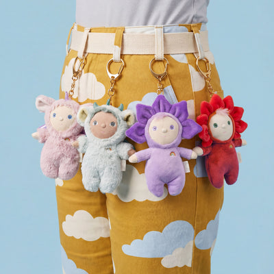 Violet plush bag charm from Dinky Dinkum Dolls clipped to mustard cloud print pants alongside three colorful Dinky charms as a playful accessory display