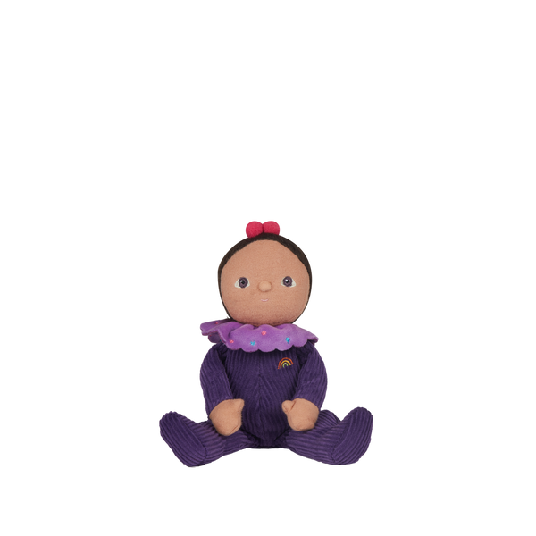 Dinky Dinkums Freya Fondant doll seated in a purple knitted outfit with a rainbow detail, brown face, and two red hair bows on a black background