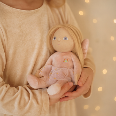 Dinky Dinkum Dolls Fairy Fiona held in a child’s arms, with soft blonde hair, a pink dress, a rainbow detail, and a gentle smiling face.