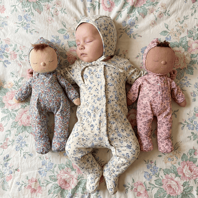 Sleeping baby in a floral hooded sleeper cuddled between two soft floral dolls on a vintage floral quilt from Dinkum Dolls by Olli Ella