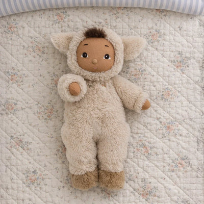 Cozy Dinkums Lamby Tig plush doll in a soft lamb costume lying on a floral quilt, featuring a warm tan face, fluffy ears, and brown hair tuft
