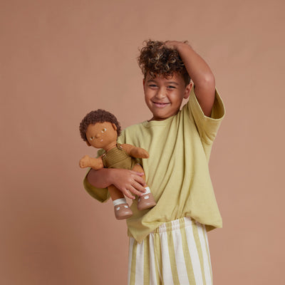 Child smiling while holding a curly haired Dinkum Dolls toy doll dressed in a striped outfit for imaginative play and cuddly adventures