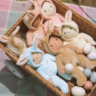 Dinky Dinkums bunny dolls in soft pastel colors nestled in a woven basket, including the Latte Bucky Bunny with floppy ears and cuddly plush bodies.