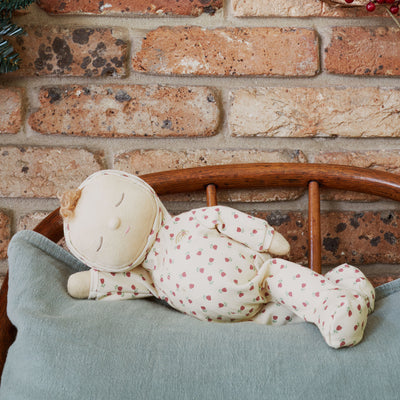 Sleeping Custard Sweetheart Dozy Dinkum doll in a floral outfit, resting on a soft blue cushion in a wooden chair. From Dinkum Dolls by Olli Ella