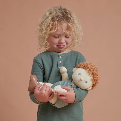 Child cuddling a Dinkum Dolls toy with soft curly hair and a cream outfit, showcasing imaginative play for toddlers and young children.