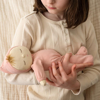 Child cuddling a soft pink Dozy Dinkums Moppet doll, gently cradling the posable baby toy in both hands indoors.