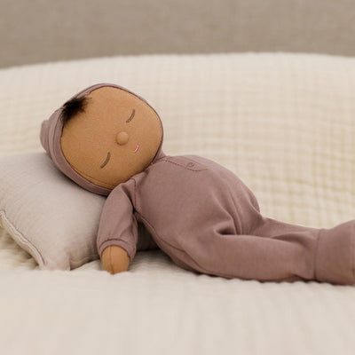 Lavender Dozy Dinkum Pip doll from Dinkum Dolls by Olli Ella lying peacefully on a cream pillow and bedding with a soft body and embroidered sleepy face