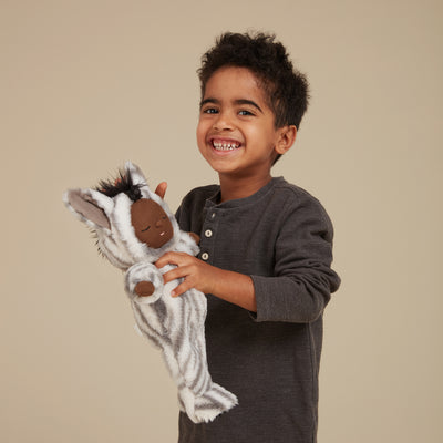 Smiling child cuddling a soft striped Cozy Dinkums Zebra Mini plush toy in a cozy dark shirt against a neutral background