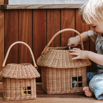Child playing with a large handmade rattan house basket with a sturdy handle and window opening beside a smaller matching basket from Olli Ella Kids Rattan