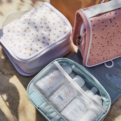 Olli Ella Kids Steel Blue wash bag open with toiletries beside patterned pink and lavender travel wash bags for kids’ sleepovers and adventures