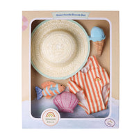 Boardwalk Beach Set by Dinkum Dolls, a wooden toy set displayed inside its kraft paper packaging. The set includes a woven straw hat with a mint green brim, a peach and white striped swimsuit with a small rainbow patch, a pink seashell, a striped fish, and a light blue ice cream cone.