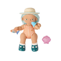 A wooden doll with light blue hair, wearing a straw hat, orange and white striped swimsuit, and teal boots, holding a toy fish and ice cream cone. A pink seashell accessory is shown next to it on a white background.