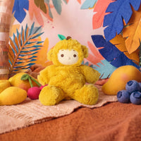 Yellow plush Mango Monkey doll with a cream face, seated among mangoes, blueberries and cherries on a colorful tropical backdrop by Dinkum Dolls by Olli Ella