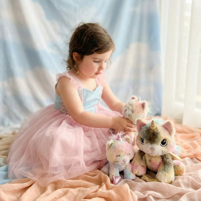 Child in a pink dress playing with plush toys on a soft surface