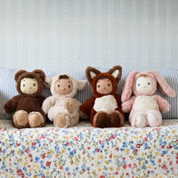 Four plush toys in animal costumes sitting on a floral-patterned couch with a striped wall in the background.