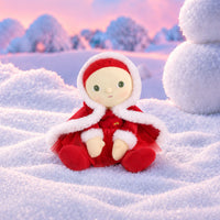 Plush doll with red hair, embroidered green eyes and rosy cheeks, wearing a red velvet hooded cape with white fluffy trim over a red outfit with a tulle skirt, white fluffy cuffs and a small rainbow patch on the chest.