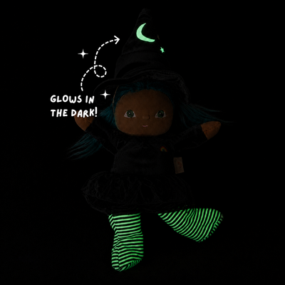 A dark-themed plush doll dressed as a witch, wearing a black hat with a glowing green crescent moon and black dress. The doll has blue hair and glowing green striped socks.