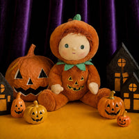Jules Jack o Lantern plush doll from Dinkum Dolls by Olli Ella sits among carved pumpkins and spooky wooden houses in a warm Halloween display