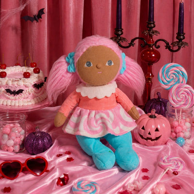 Dinky Dinkum Lottie Lollipop doll with pink pigtails, a candy swirl dress and turquoise leggings surrounded by lollipops, cupcakes and pink Halloween decor
