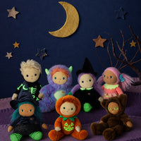 Dinky Dinkum Lottie Lollipop doll with pink hair and a coral outfit surrounded by colorful dolls under a crescent moon and stars in a cozy woodland scene