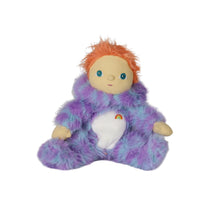 Purple and blue fuzzy monster doll with bright orange hair, blue eyes, tan face and hands, and a white belly featuring a small rainbow emblem