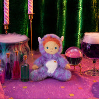 Purple fuzzy Miles Monster doll with orange hair and a white belly sits among colorful potion bottles and sparkling star confetti. Dinkum Dolls by Olli Ella.