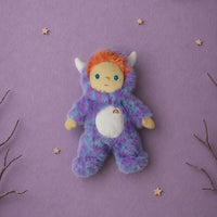 Fuzzy purple and blue Miles Monster plush with orange hair white horns and rainbow belly patch on a lavender background with stars from Dinkum Dolls by Olli Ella