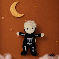 Dinky Dinkum Scully Skeleton plush doll in a black bone-print costume, surrounded by stars, a crescent moon, and a spider on a warm brown backdrop.