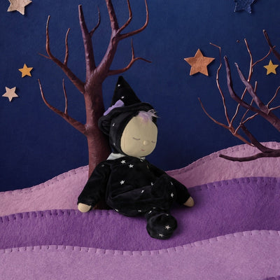 Sleepy Dozy Dinkum Willa witch doll in a black starry outfit and pointed hat seated among purple hills and bare trees under a starry night sky