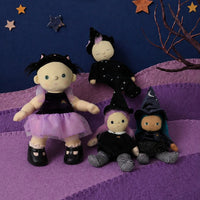 A sleepy black witch doll from Dinkum Dolls by Olli Ella sits with three other dolls on a purple quilt, surrounded by stars and whimsical Halloween decor