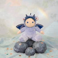Stuffed toy in a purple outfit with wings and horns on rocks with a starry background