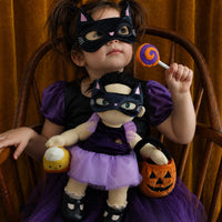 Child in a cat costume holds a Dream Dinkum doll dressed as a witch with a pumpkin basket, lollipop and purple tutu by Dinkum Dolls by Olli Ella
