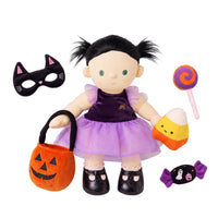 Dream Dinkum Doll Mabel Moon in a purple witch costume with pigtails, holding a lollipop and pumpkin basket, shown with a cat mask, candy corn, and wrapped candy.