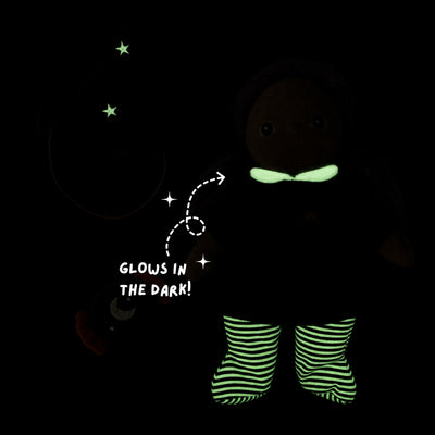 A dark plush doll or toy figure wearing glow-in-the-dark striped socks and a glowing green bow tie, shown on a black background with a wizard hat outline and text reading 'GLOWS IN THE DARK!'.