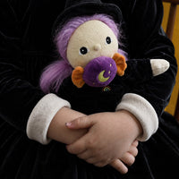 Child holding Willa the Witch doll with purple hair, a black witch costume, white cuffs, and a purple bat toy by Dinkum Dolls by Olli Ella