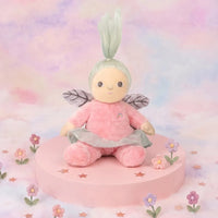 Plush fairy toy with pink outfit and green hair on a pastel background