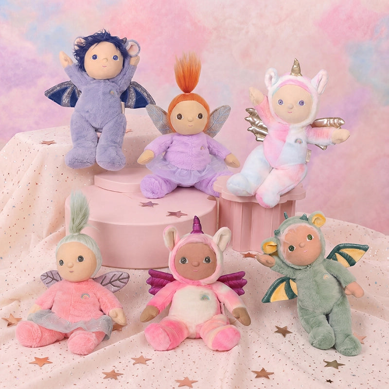 Six colorful Dinky Dinkums plush dolls, including a pink and white unicorn, sit and pose on pastel pink blocks against a dreamy starry backdrop.