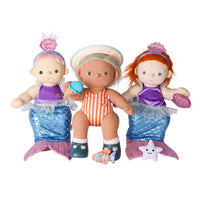 Three mermaid-themed dolls or plush toys arranged together on a plain white background. The center doll wears an orange-and-white striped one-piece, a white hat, and teal shoes, holding a blue shell.