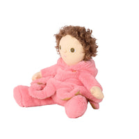 A plush doll with curly brown hair wearing a soft pink robe, seated against a plain white background.