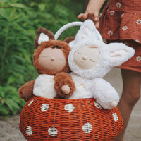 White sleeping fox plush toy beside a brown fox in a red woven basket, held by a child outdoors. Dozy Dinkums Cozy Dinkums Fenix Fox
