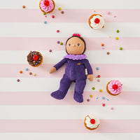 Dinky Dinkums Freya Fondant doll in a purple ribbed outfit with a pink collar, surrounded by colorful sweets and cupcakes on a pink striped background