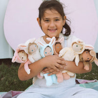 Smiling child cuddling a group of soft Dinky Dinkums bunny dolls in pastel colors, including Babs Bunny in apricot, outdoors on a grassy lawn