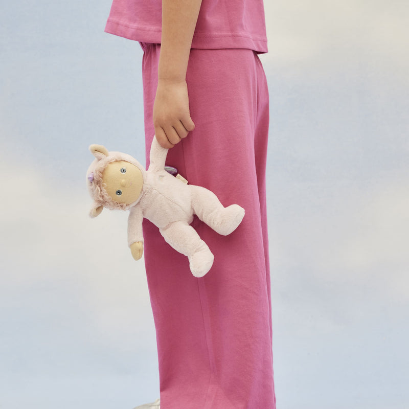 Child in pink clothing holds a soft cream Una unicorn doll with a blush pink mane, embroidered face, and rounded limbs from Dinky Dinkums