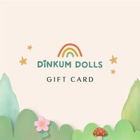 Dinkum Dolls gift card by Olli Ella featuring a rainbow, golden stars, pink flower, mushroom, and colorful pastel foliage on a soft cream background