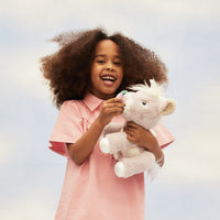 Smiling child holding Dinkum Unicorn Glimmer, a soft lilac plush unicorn with a white mane and horn from Dinkum Unicorns