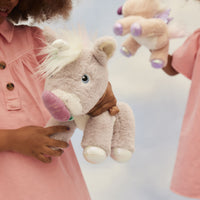 Child holding a soft lilac plush unicorn with a purple horn and white mane, while another unicorn is held in the background, from Dinkum Unicorns