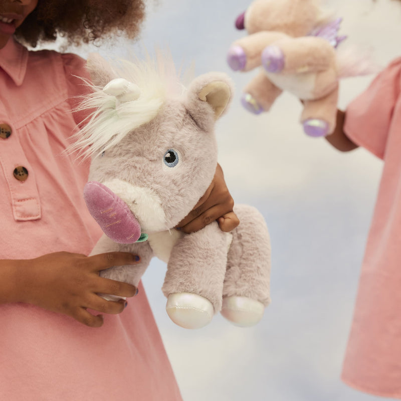 Child holding a soft lilac plush unicorn with a purple horn and white mane, while another unicorn is held in the background, from Dinkum Unicorns